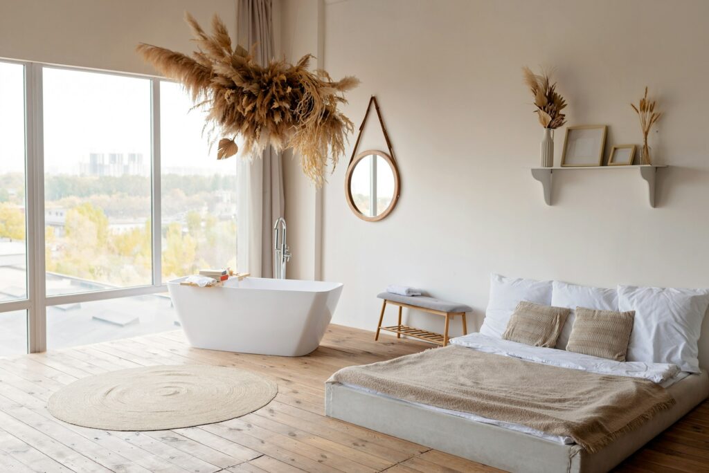 Bright modern boho chic bedroom with a freestanding white bathtub against a panoramic window